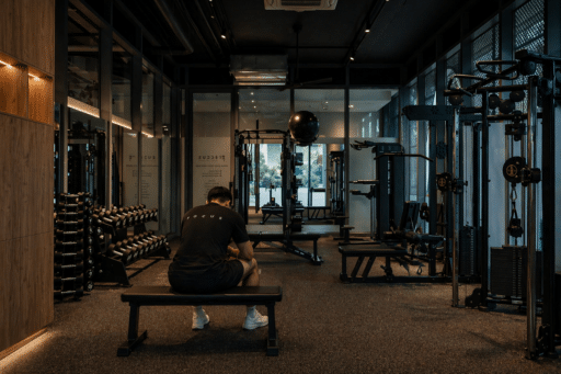 Man wearing a black shirt with 'FOCUS' on the back sits on a bench in a dimly lit gym, surrounded by weight machines and dumbbells.