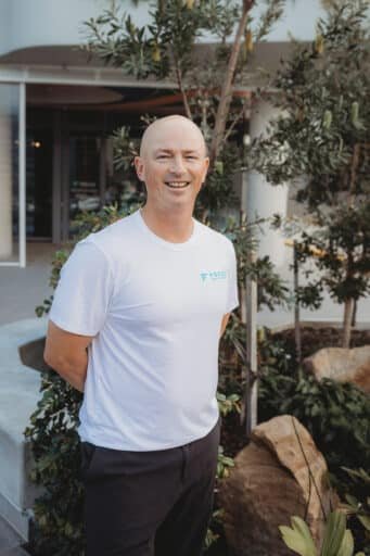 Ryan Fraser smiling in a white Focus Health & Fitness shirt, standing outside the Norwest personal training studio