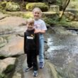 Smiling brother and sister standing on rocks by a creek in Sydney bushland, symbolising natural joy, family connection, and emotional wellbeing.