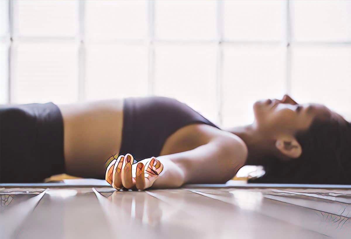 Woman lying in meditation pose on a yoga mat in natural light, symbolising rest and recovery guided by Doctor Quiet.