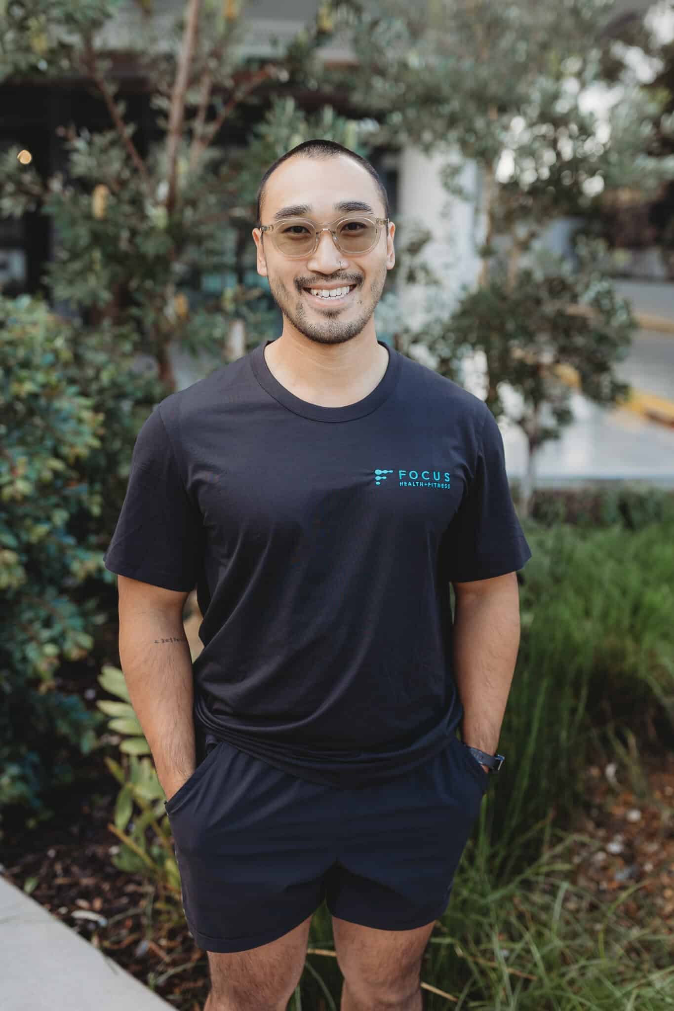 James, personal trainer at Focus Health & Fitness Norwest, standing outside the studio smiling in a team t-shirt.