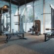 A modern gym with weight machines, benches, and large windows letting in natural light.